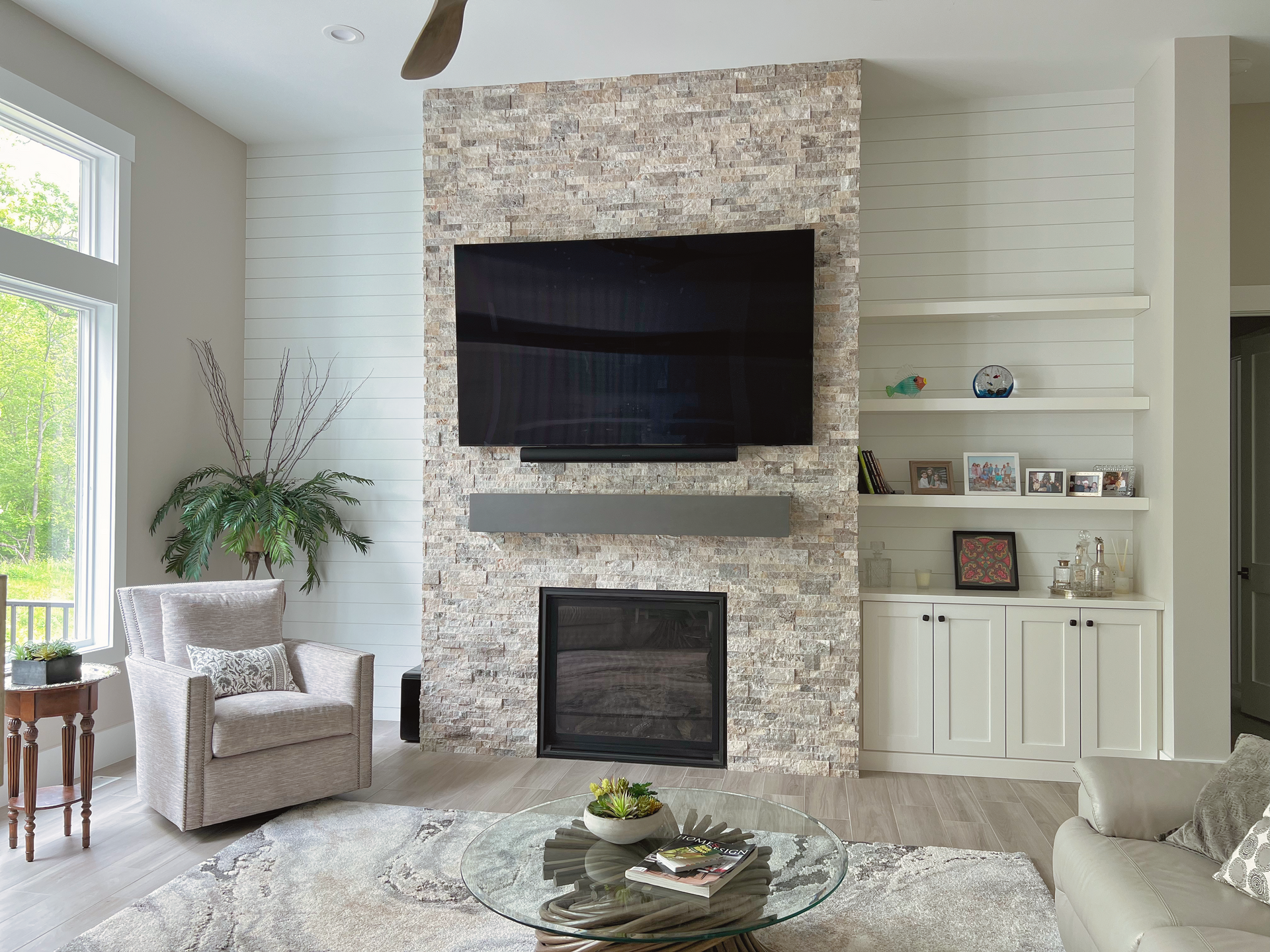 Living room with fireplace, mounted TV, built-in shelves, armchair, and sofa; neutral tones.