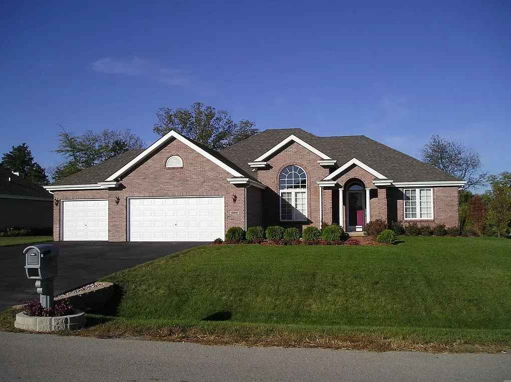 Brick house with two-car garage, arched window, and front lawn on a sunny day.