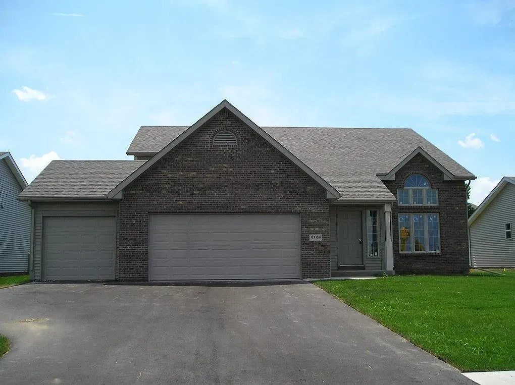 A brick home with a two-car garage and a driveway, blue sky in the background.
