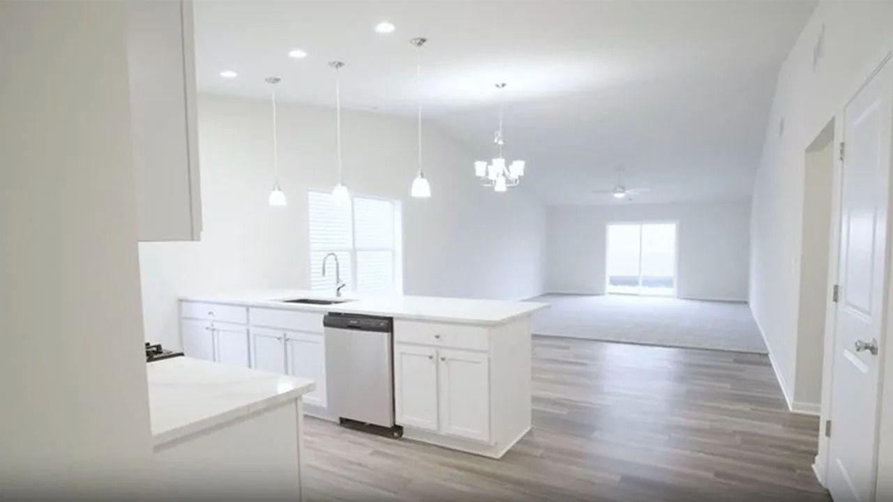 White kitchen with island, stainless steel appliances, and adjacent living area with white walls and light flooring.