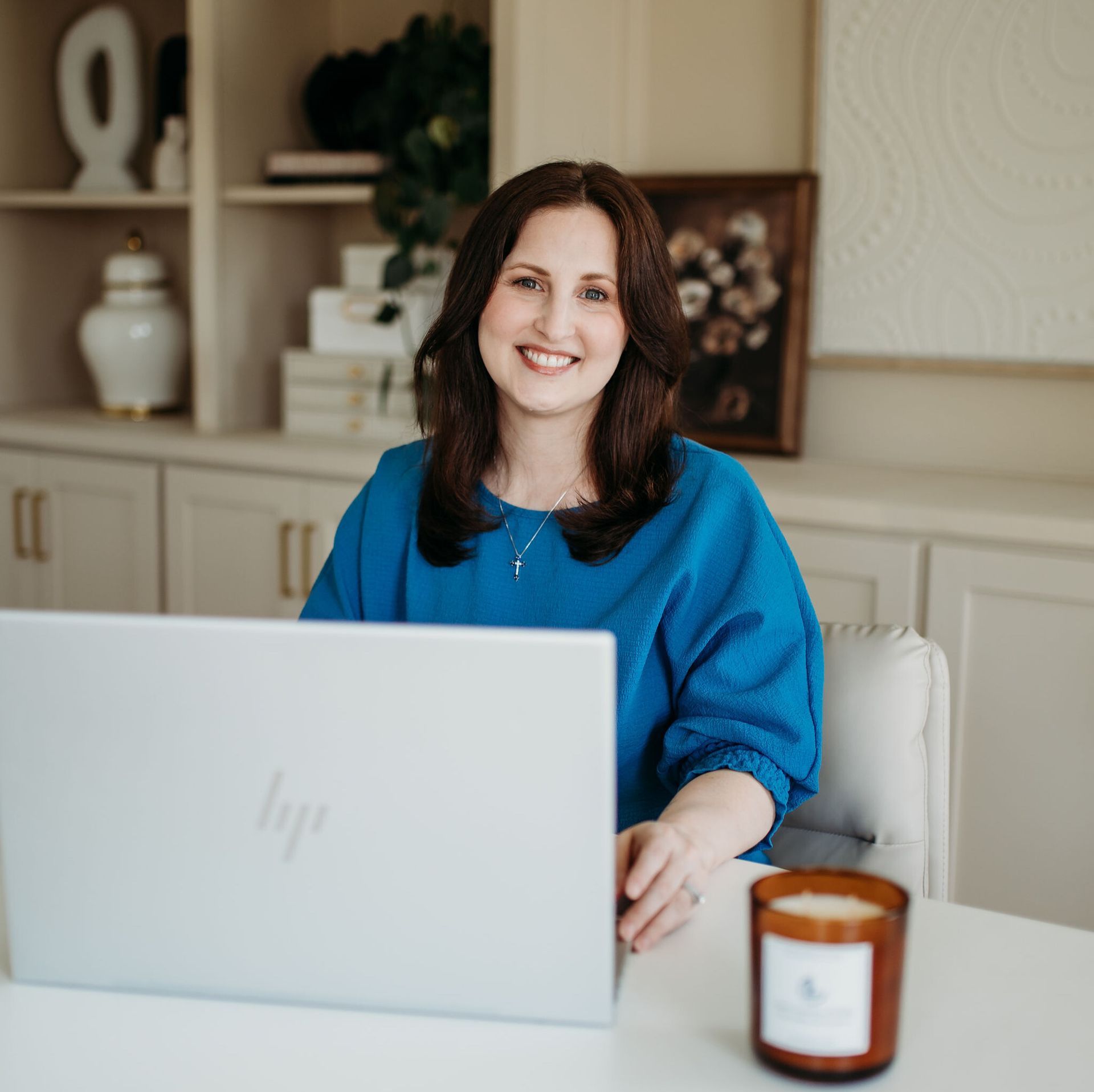 Woman smiling behind a laptop at a desk with a candle in a home office