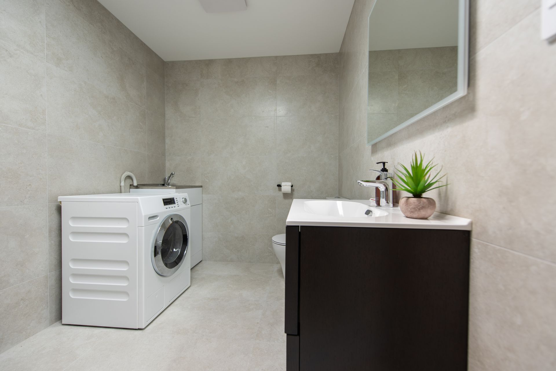 A bathroom with a washing machine , sink , toilet and mirror.