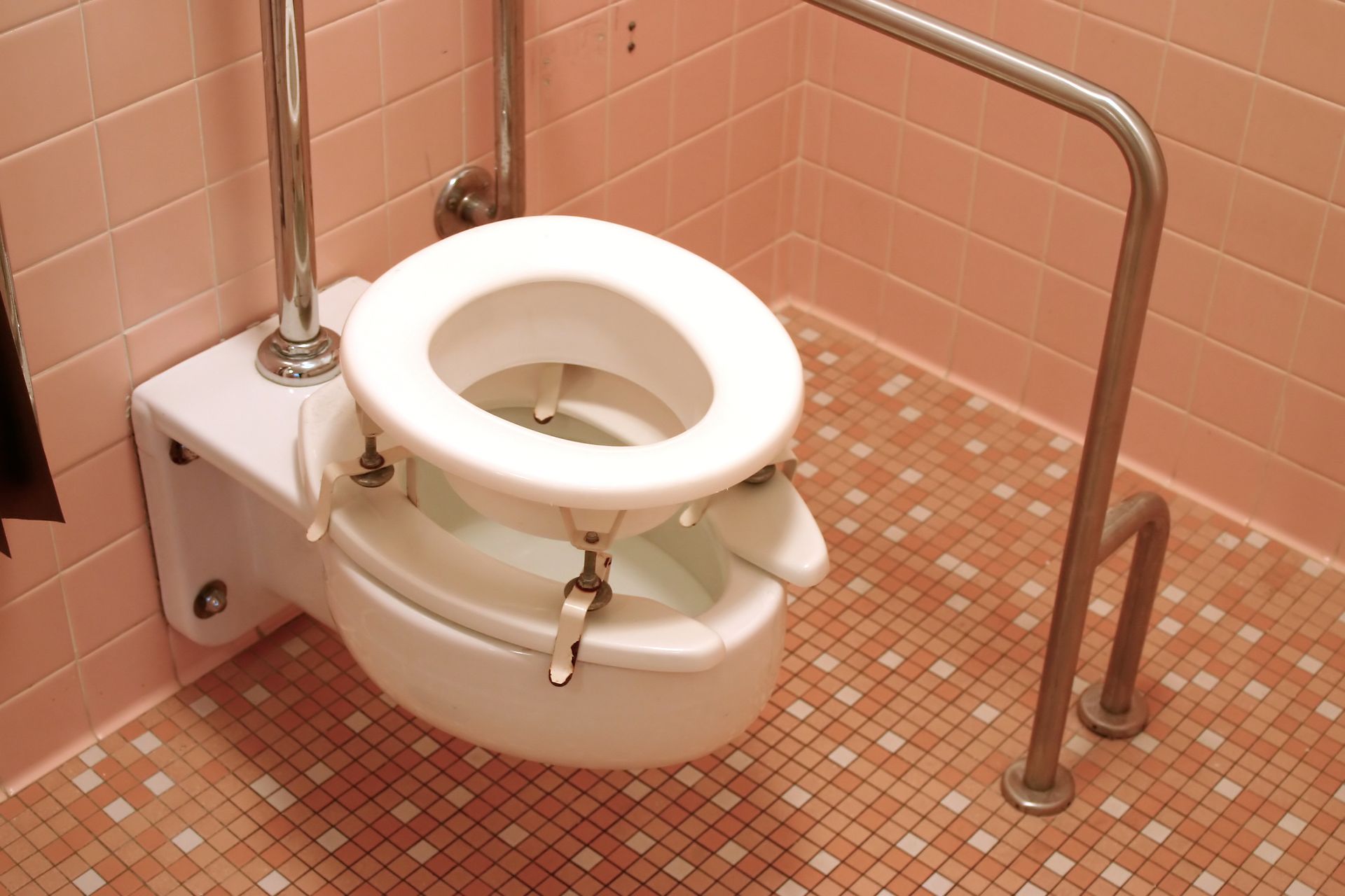 A handicapped toilet in a bathroom with pink tiles