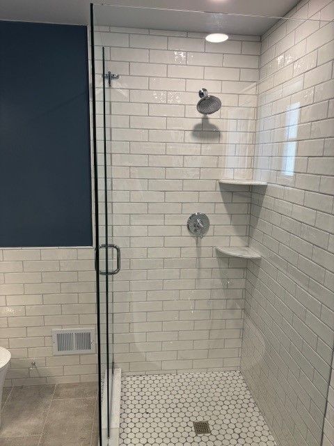 A bathroom with white tiles and a walk in shower with a glass door.