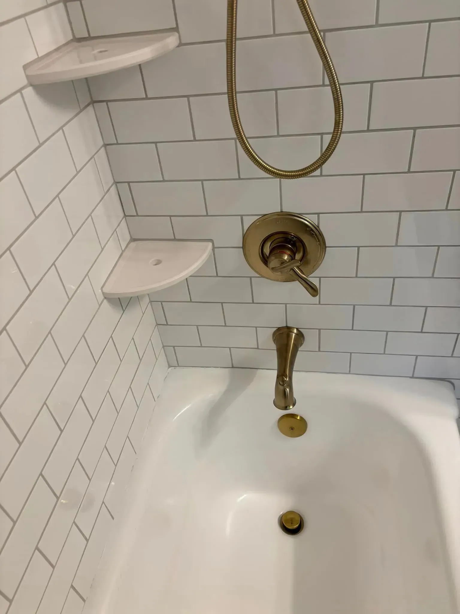 A white bathtub with a gold shower head in a bathroom.