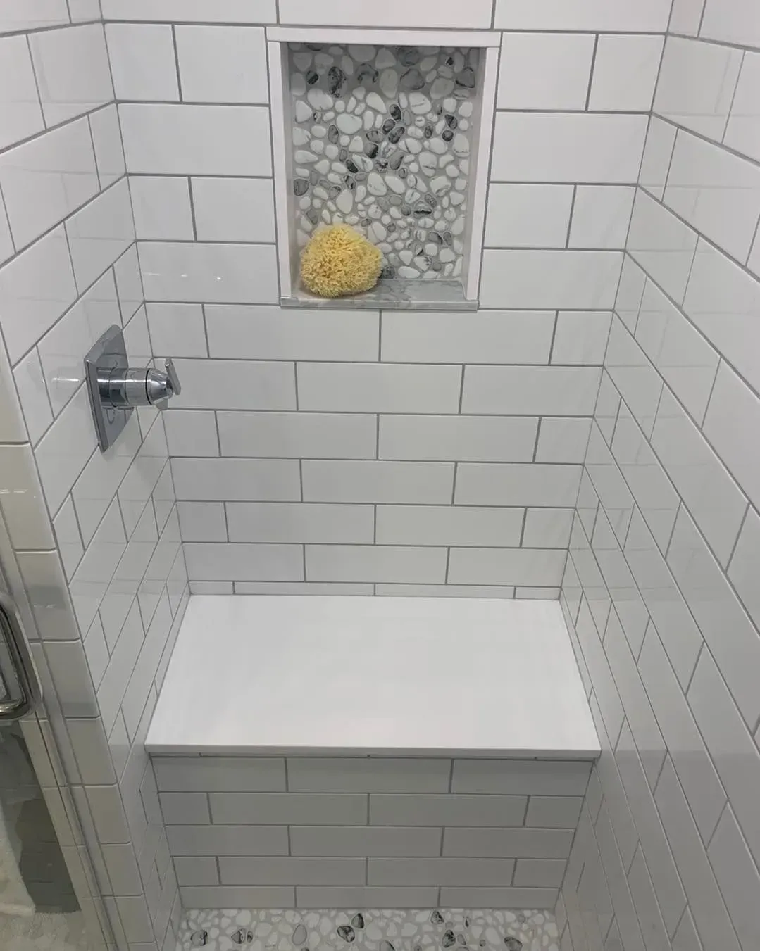 A shower with a bench and a shelf with a sponge in it.