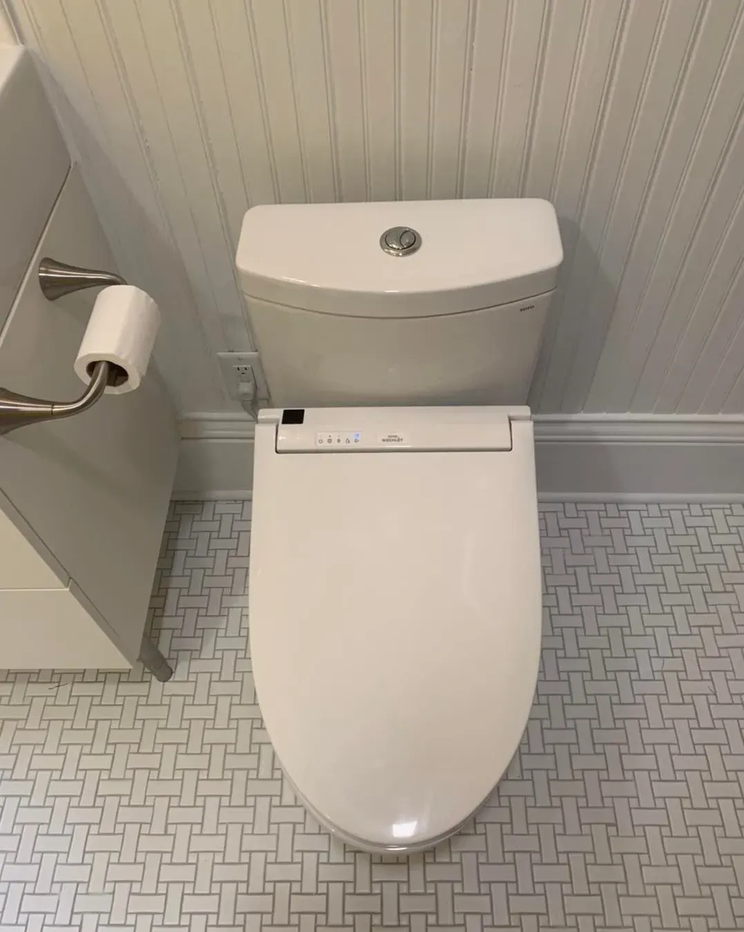 A white toilet is sitting in a bathroom next to a toilet paper roll.