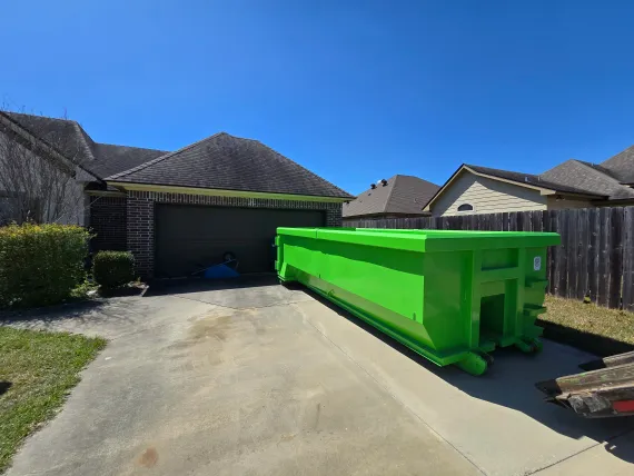 A green dumpster is parked in front of a house