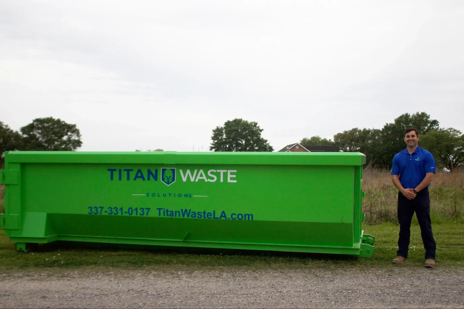 A man is standing in front of a green dumpster.