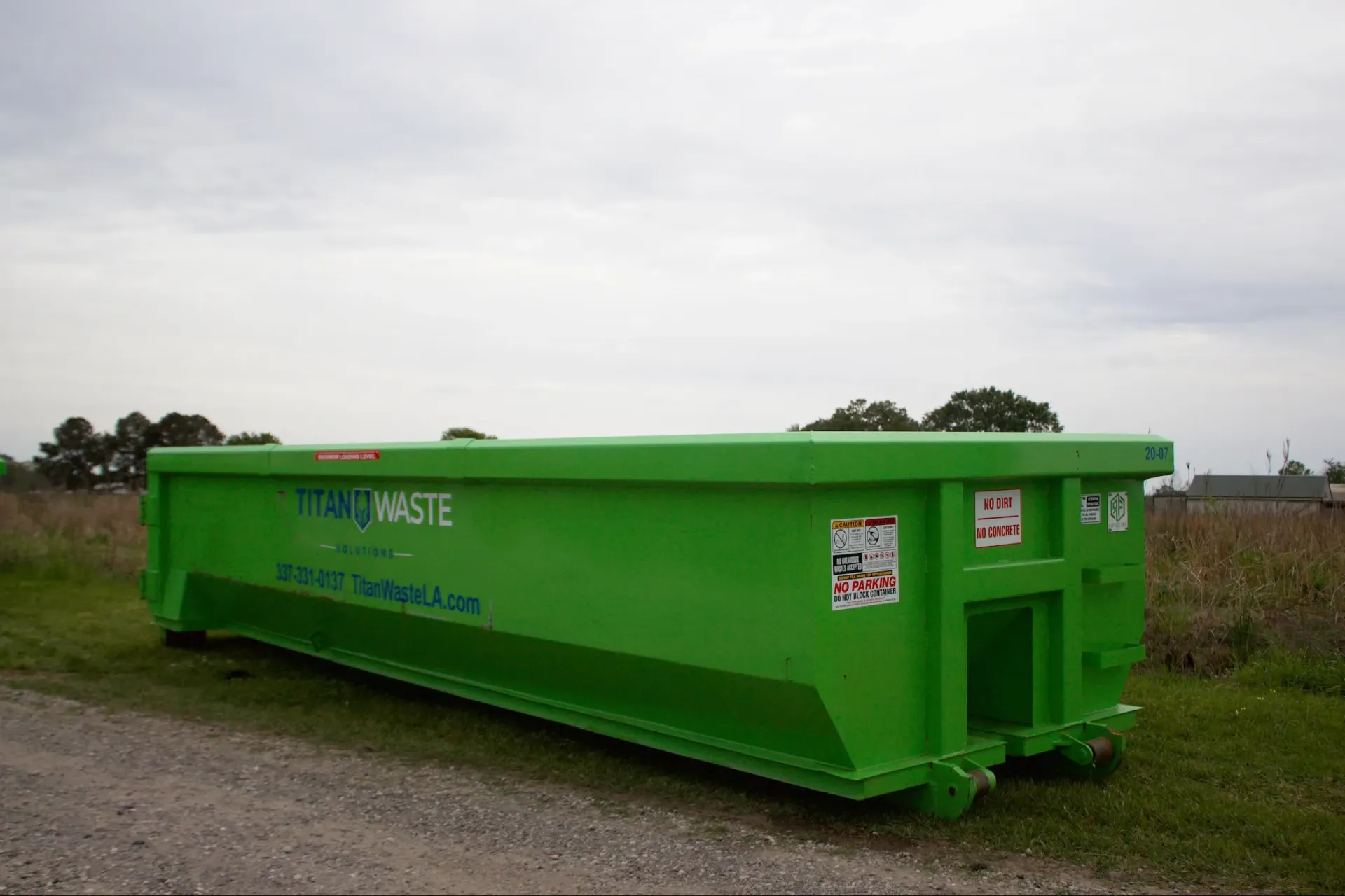 A green dumpster is parked in a grassy field.