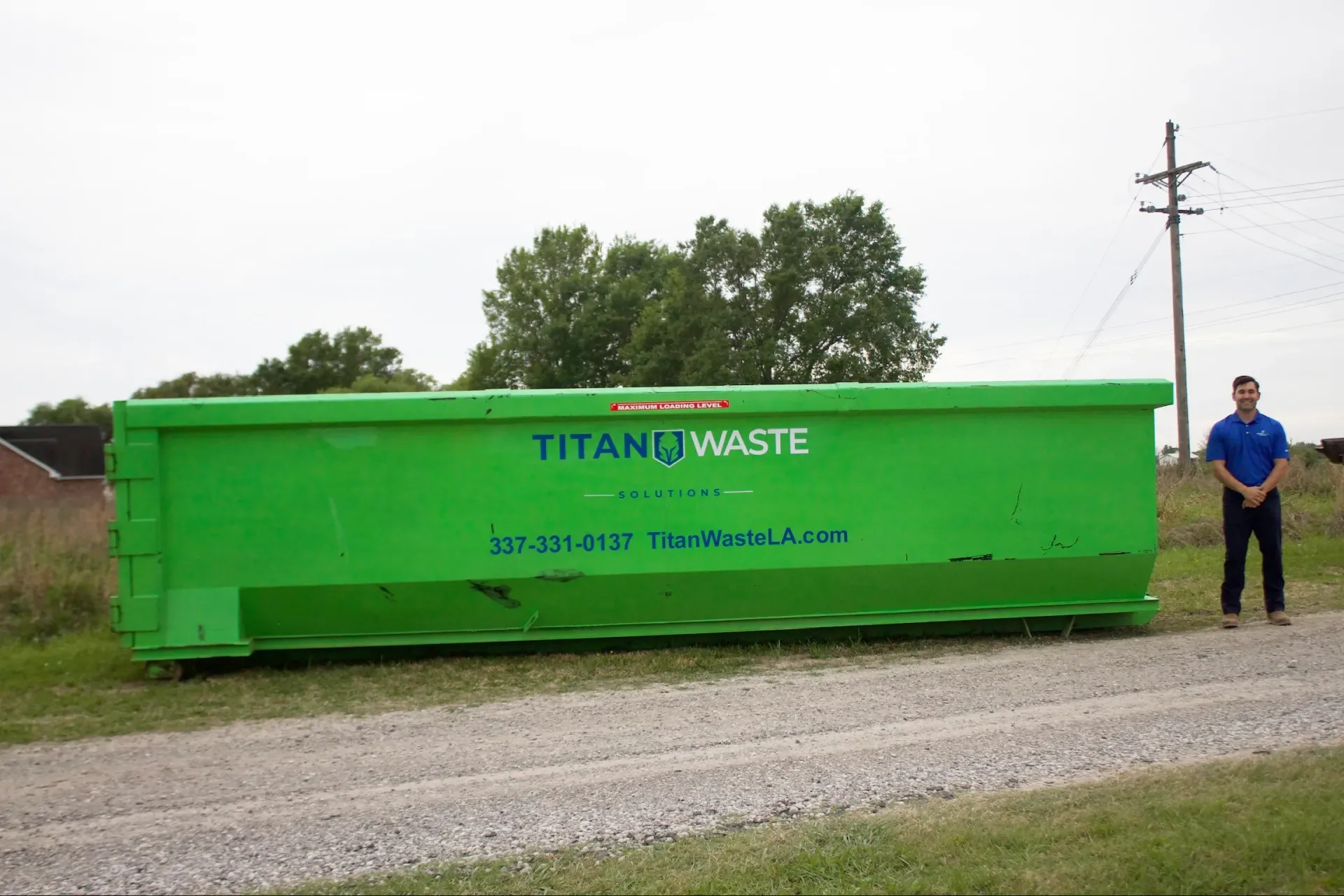 A man is standing next to a large green dumpster.