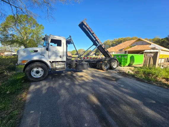A dump truck is parked on the side of the road next to a green dumpster.