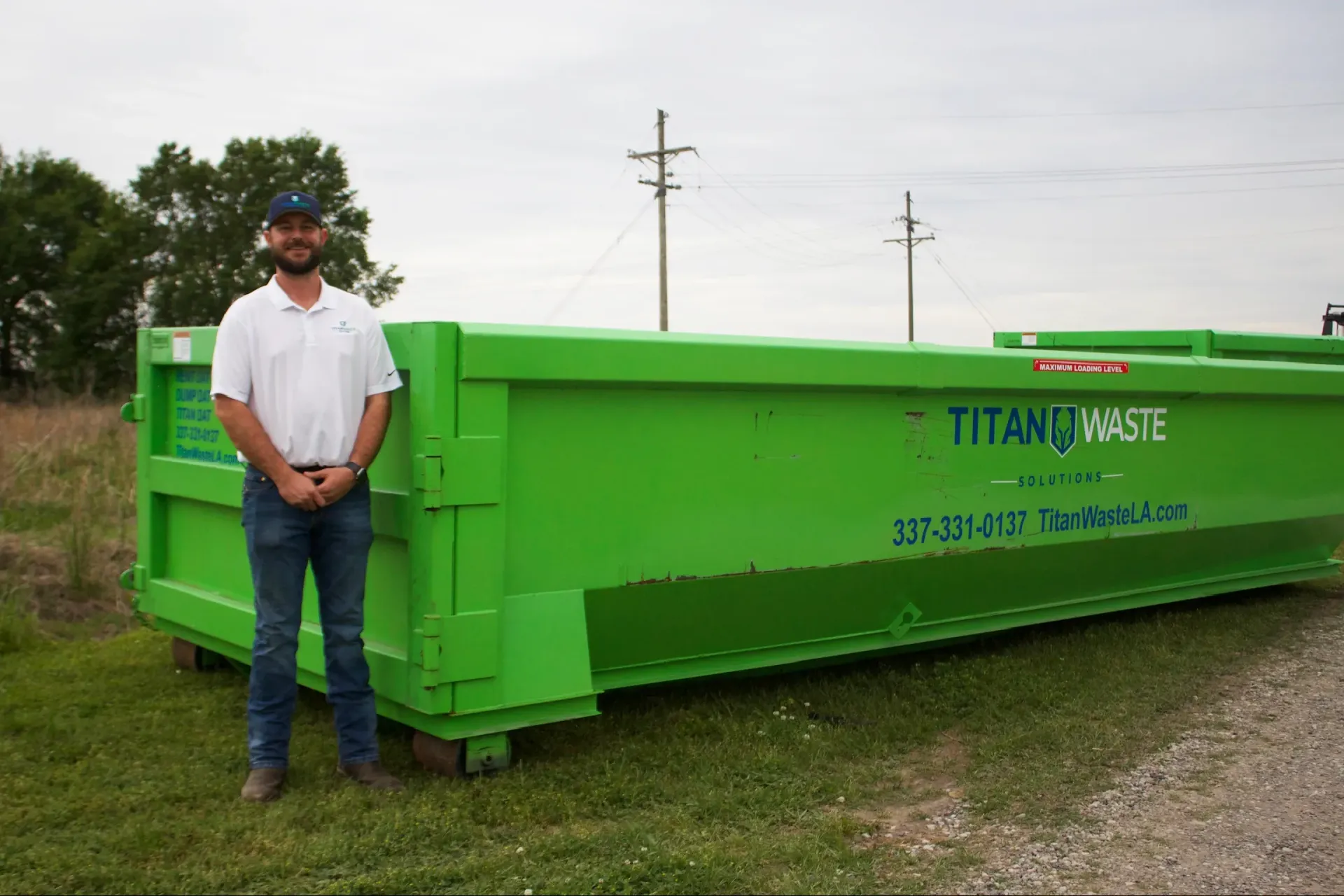 A man is standing in front of a green dumpster.