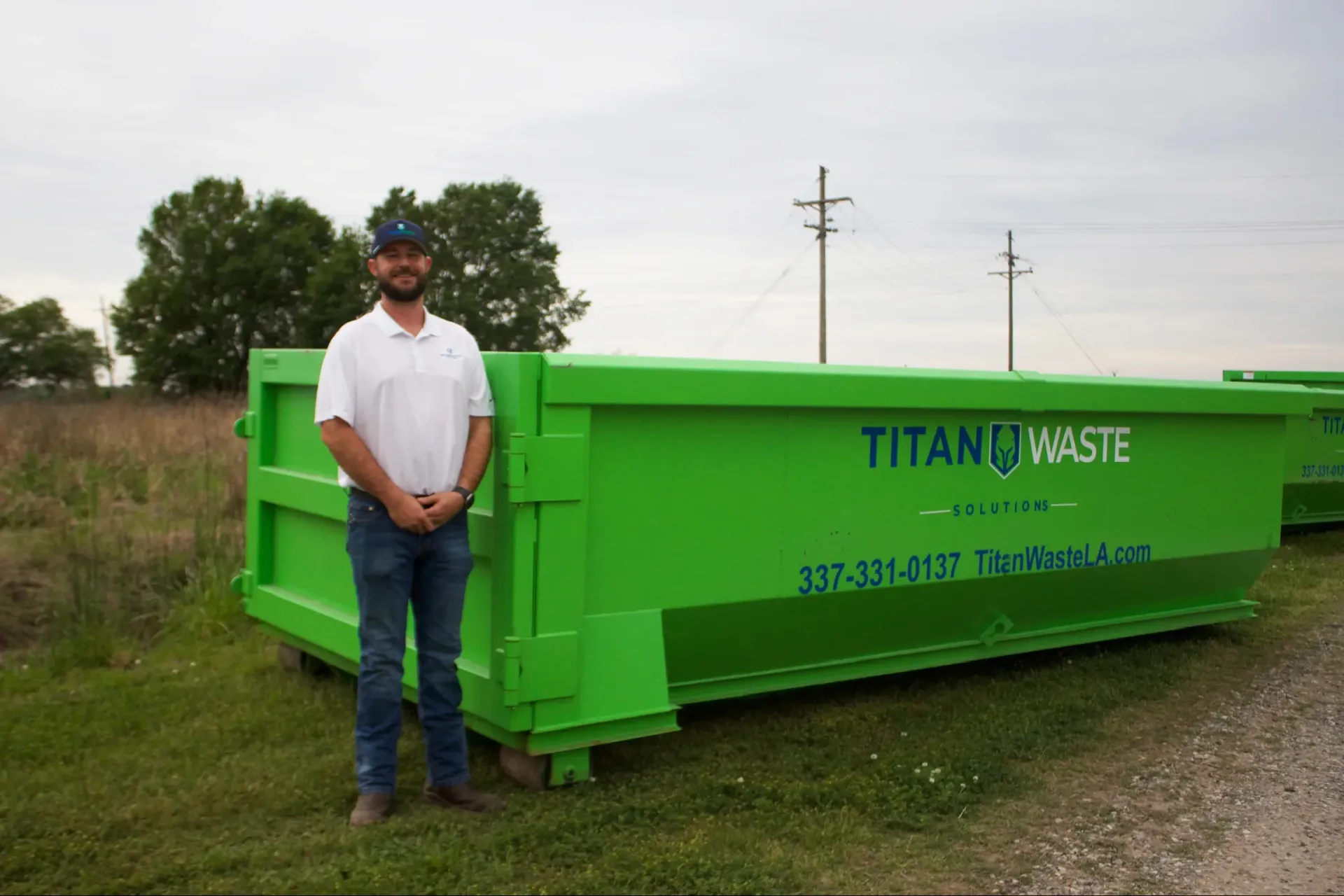 A man standing next to a green dumpster that says titan waste