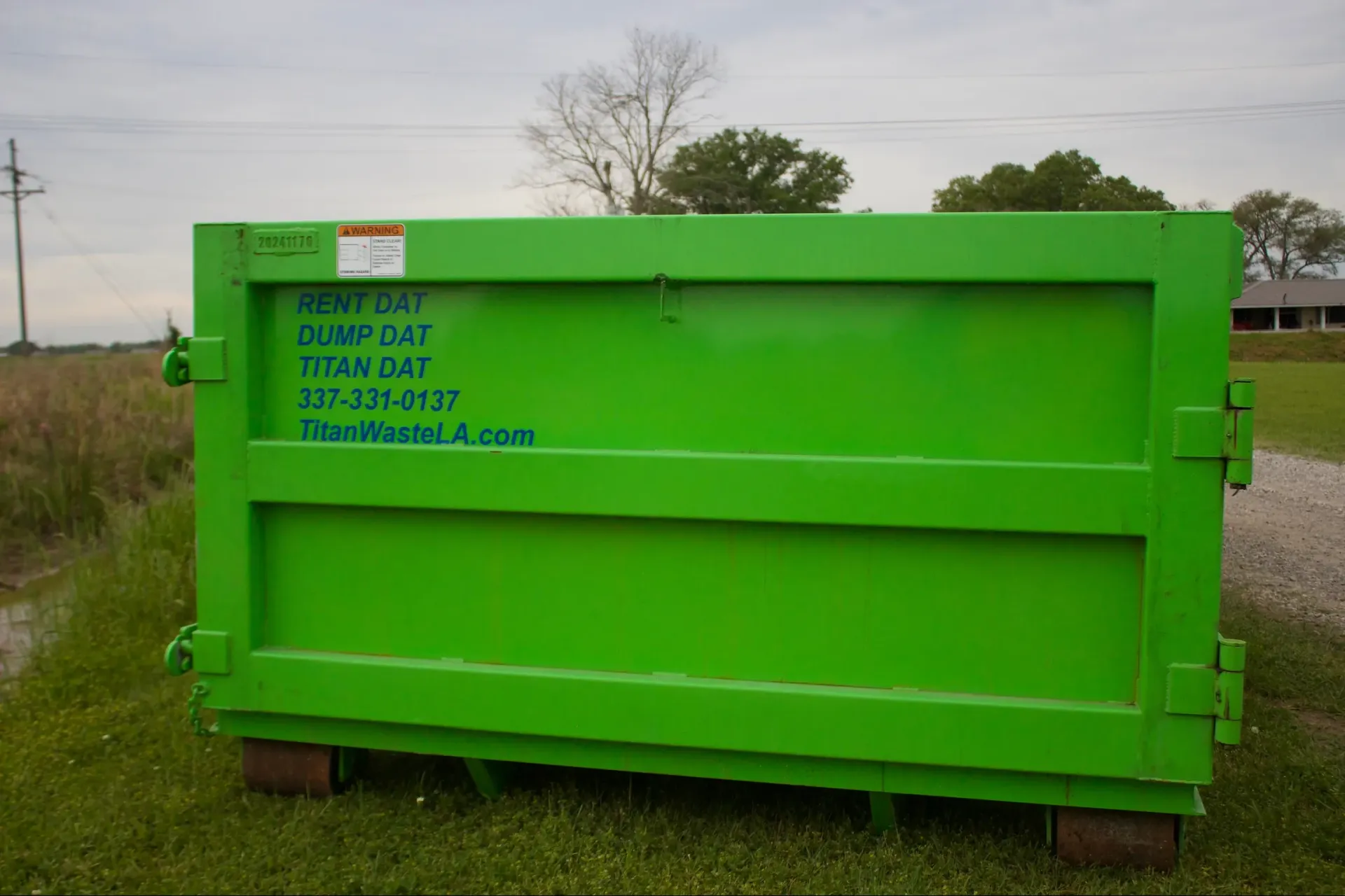 A green dumpster is sitting in the middle of a grassy field.