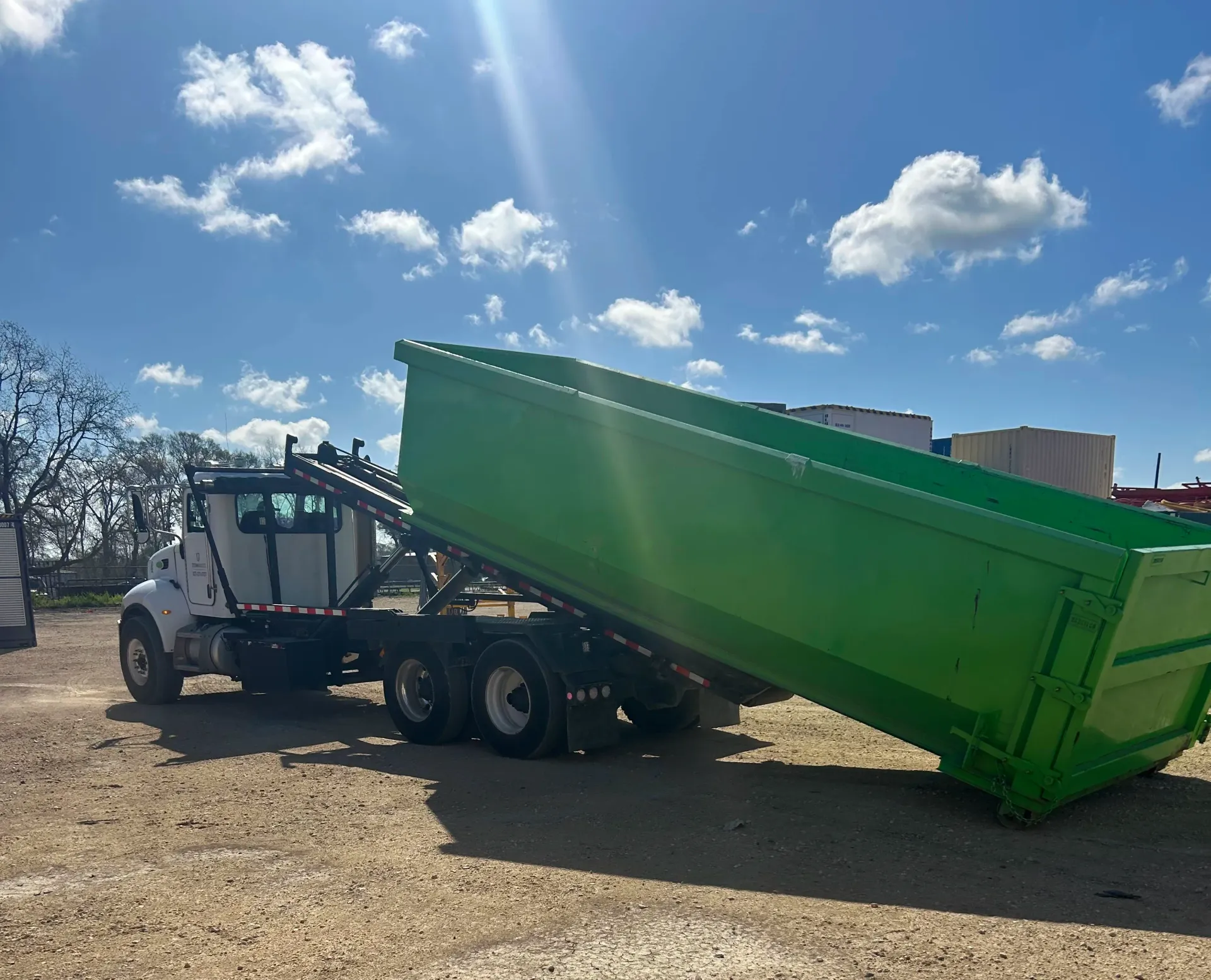 A green dumpster is being towed by a white truck.