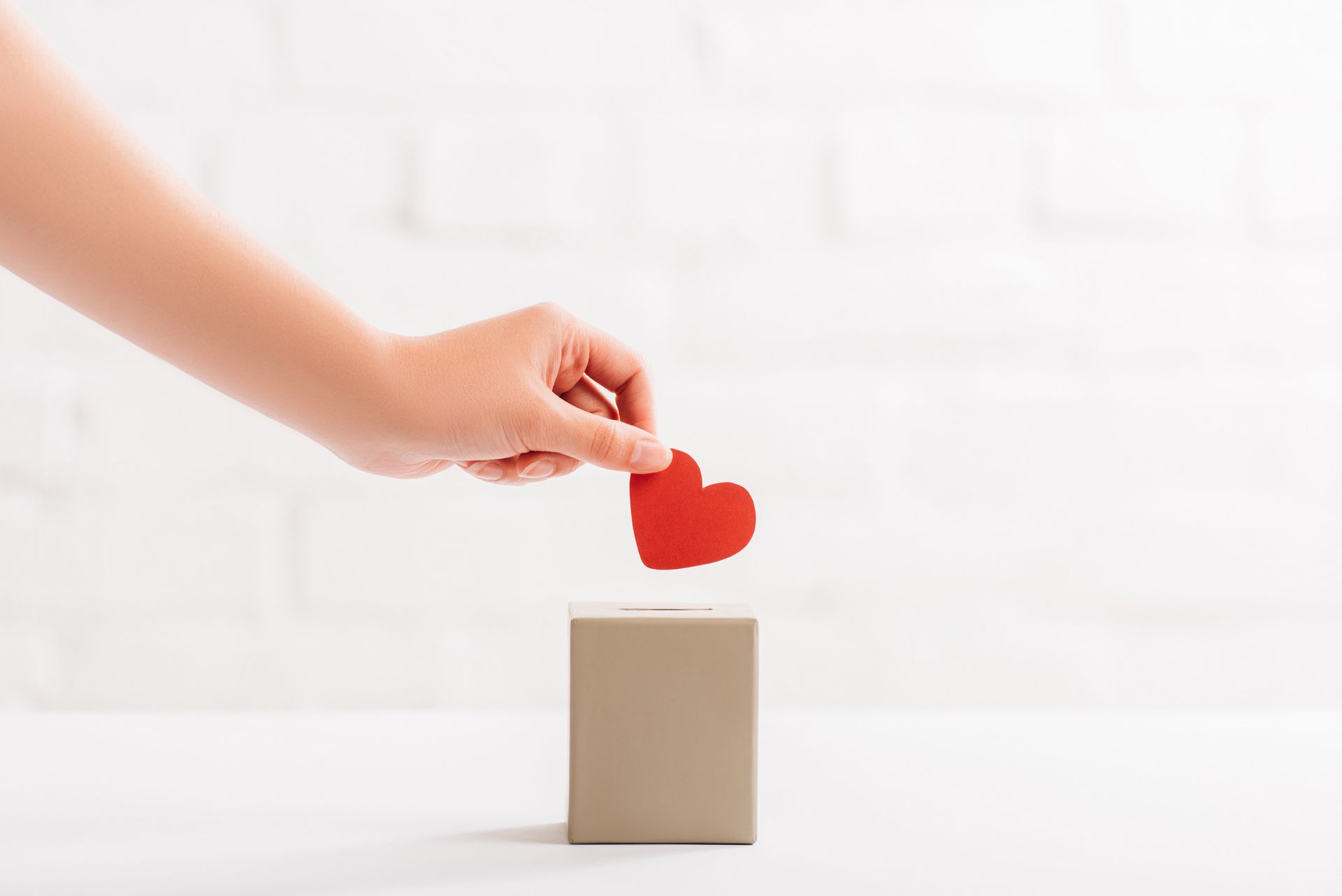 Hand placing a red heart on a beige box against a white background
