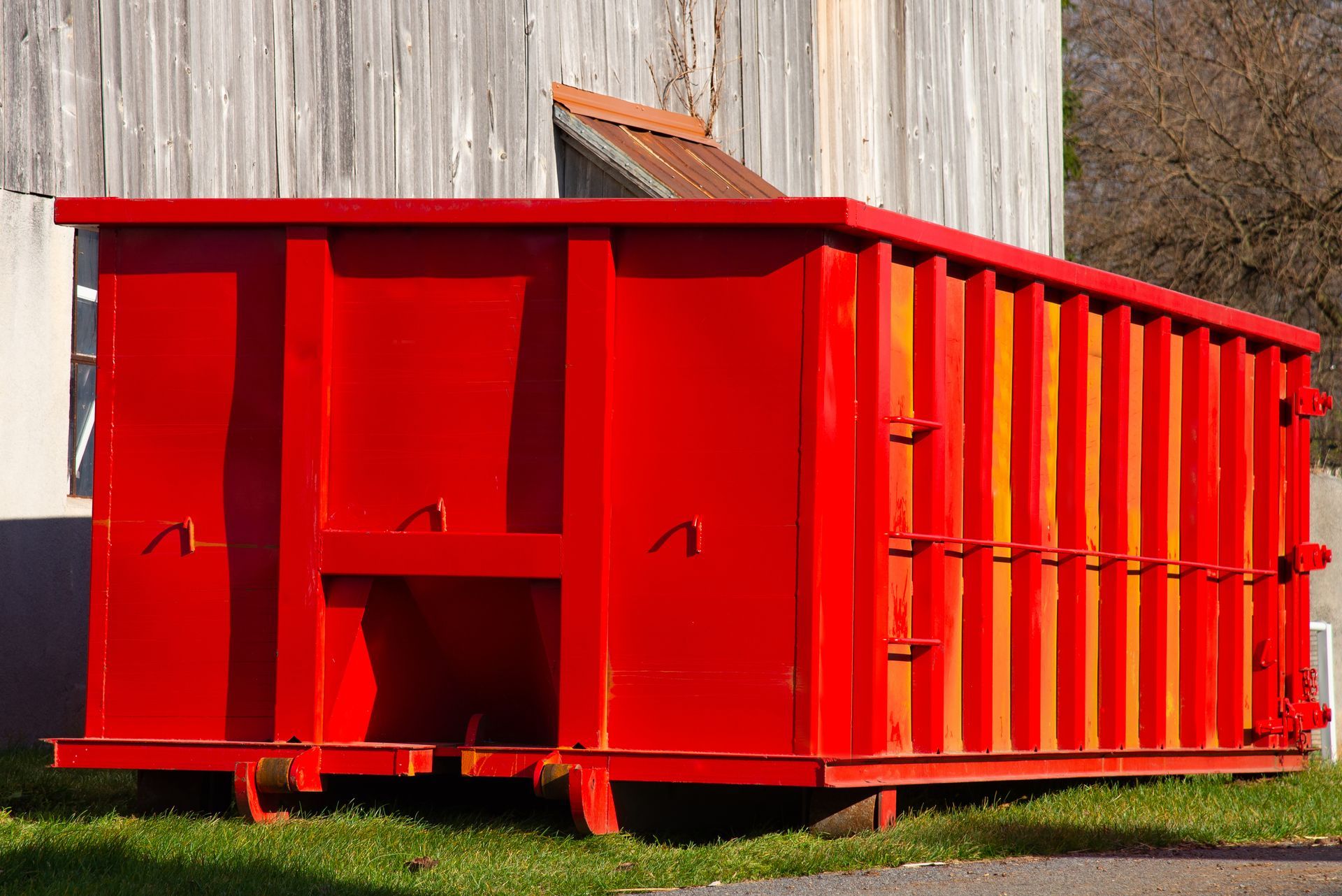 Bright red dumpster beside a weathered wooden building on grass