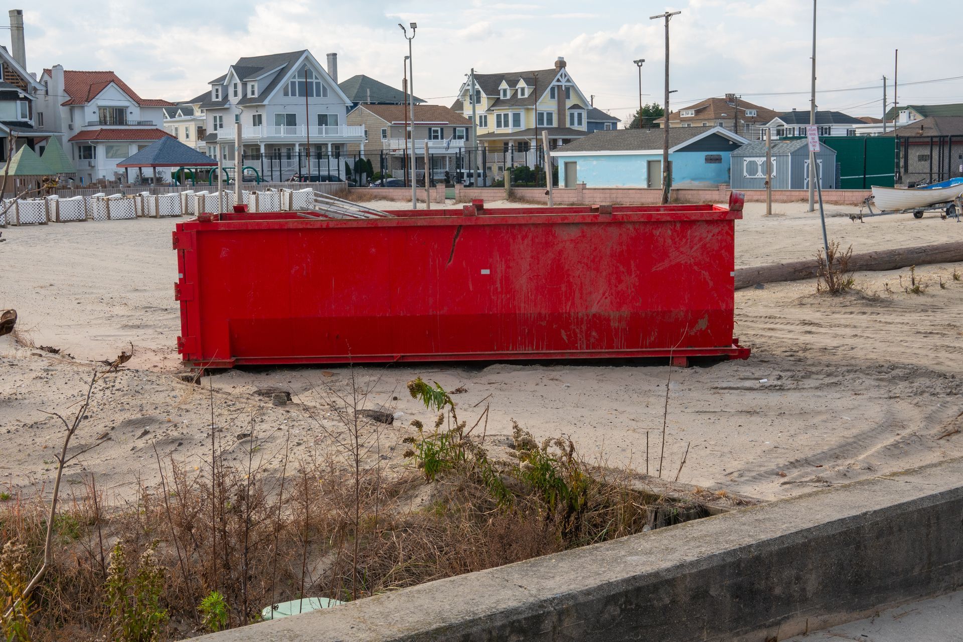 Red dumpster on a sandy beach with houses in the background