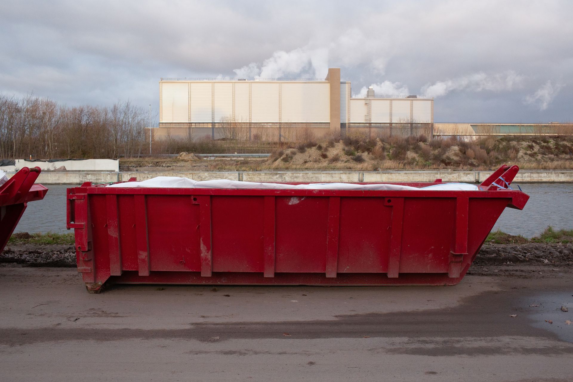 Red construction dumpster on pavement with a large industrial building in the background