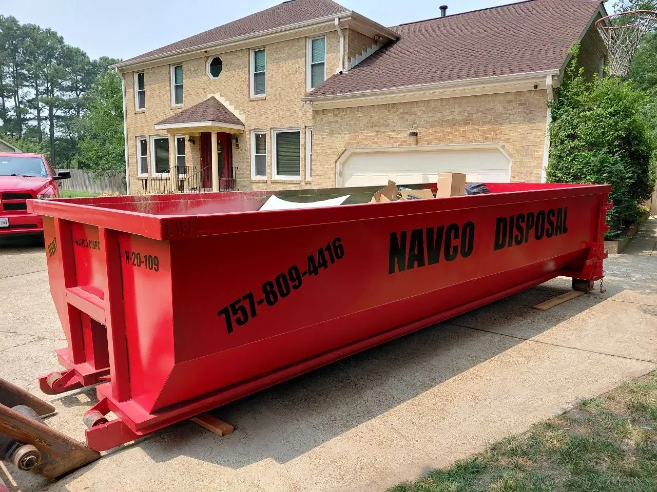 Red dumpster filled with rubble on a dirt roadside near trees