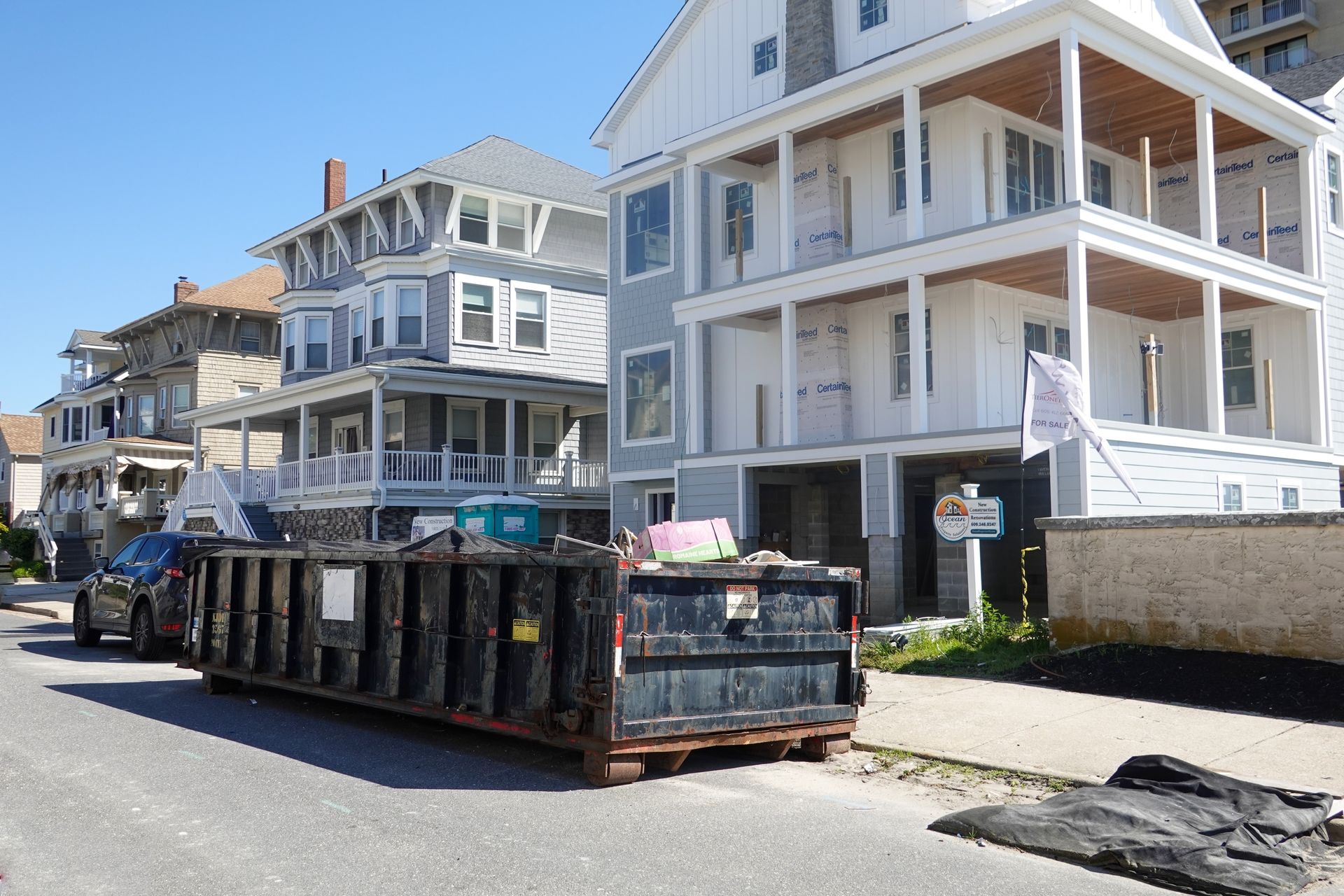 Street with beach houses and a large construction dumpster in front under a clear blue sky