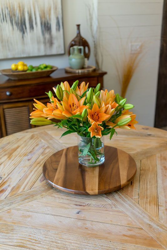 Orange flowers in a glass vase on a round wooden table in a bright dining room