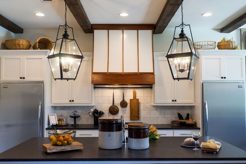 Modern kitchen with white cabinets, stainless steel fridges, black island, and hanging lantern lights.