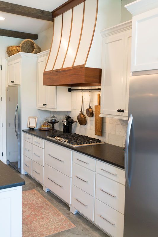 Bright kitchen with white cabinets, black countertop, wood range hood, and stainless steel refrigerator