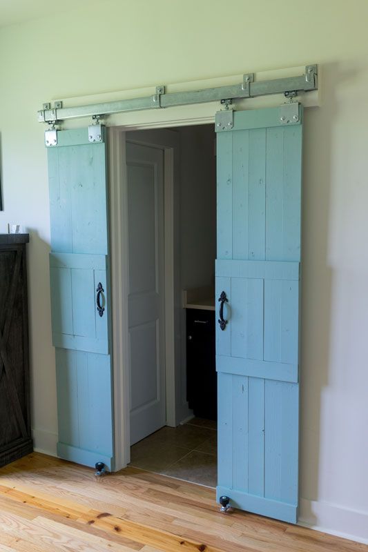 Blue sliding barn doors open to a doorway in a light-colored room with wood floors.