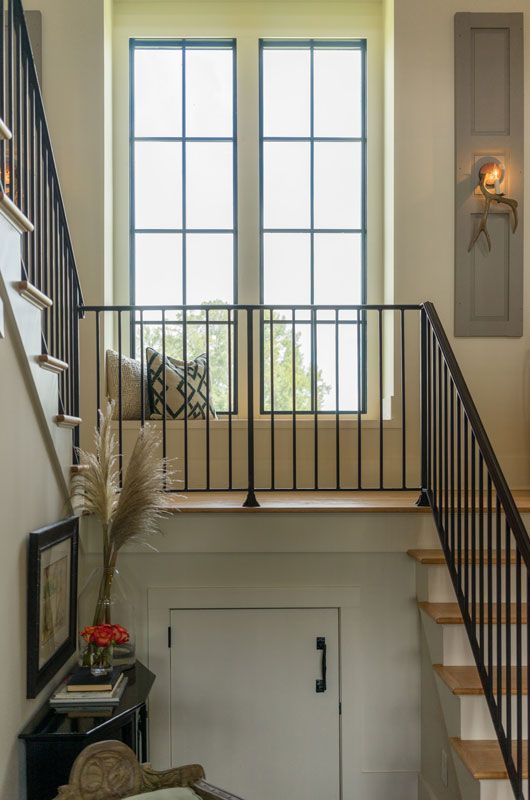 Bright stairwell with large windows, black railing, and a hanging wall sconce above a lower door.