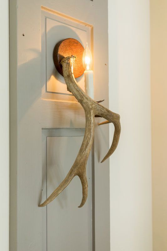 Wall sconce with amber glass and antler-like decorative arms on a white paneled wall