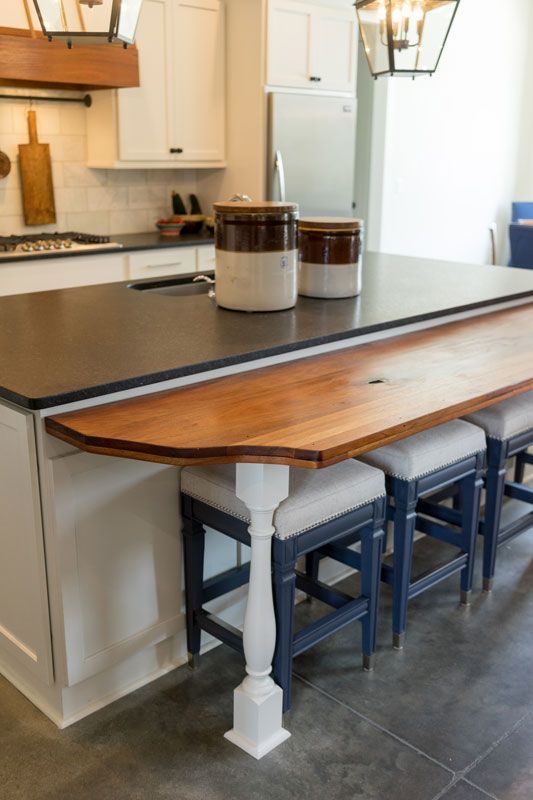Kitchen island with butcher-block extension, dark countertop, and two stools beneath it.
