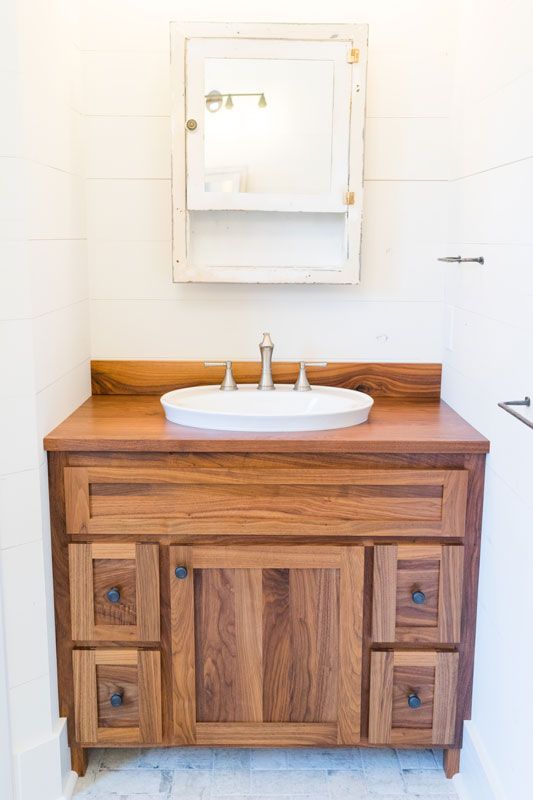 Wooden bathroom vanity with white sink and mirror on a light wall