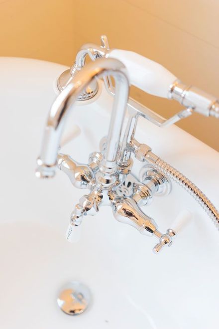 Chrome bathtub faucet with handheld showerhead over a white tub against a beige wall
