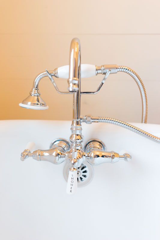 Chrome clawfoot bathtub faucet with handheld shower head against a white tub wall