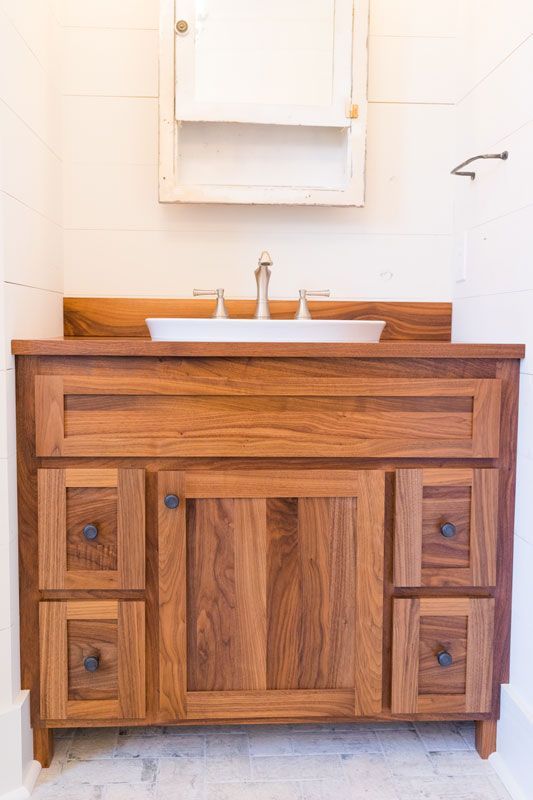 Wooden bathroom vanity with white sink and mirror against a light wall