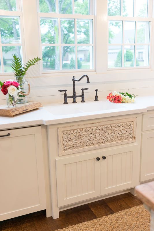 Bright kitchen sink under large windows with white cabinets and flowers on the counter