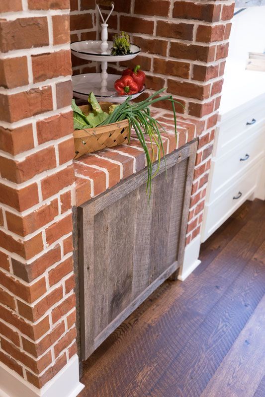 Brick fireplace nook with rustic cabinet, shelves, plants, and hardwood floor