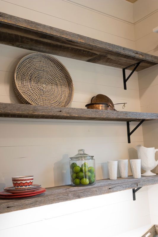 Rustic kitchen shelves with woven basket, serving dishes, glass jar of limes, cups, and teapot