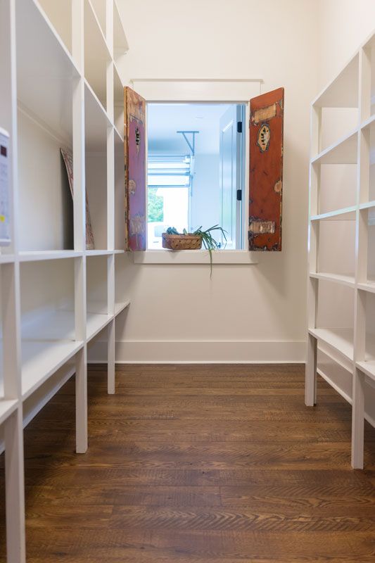 Narrow walk-in closet with white shelves on both sides, wood floor, and a window at the far end.