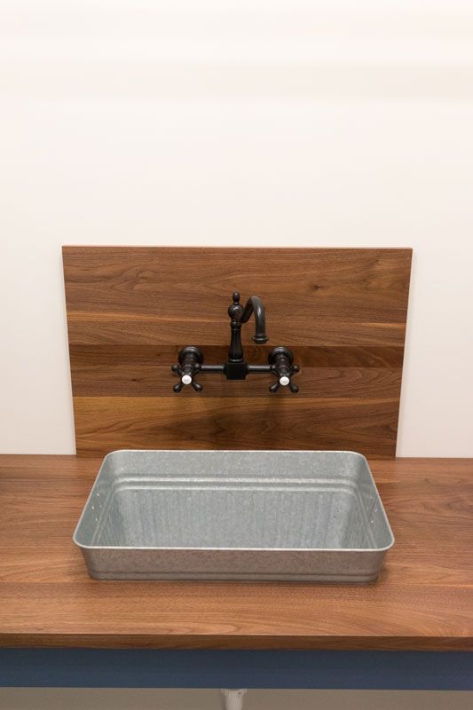 Metal sink basin on a wooden counter with a black faucet against a plain wall.