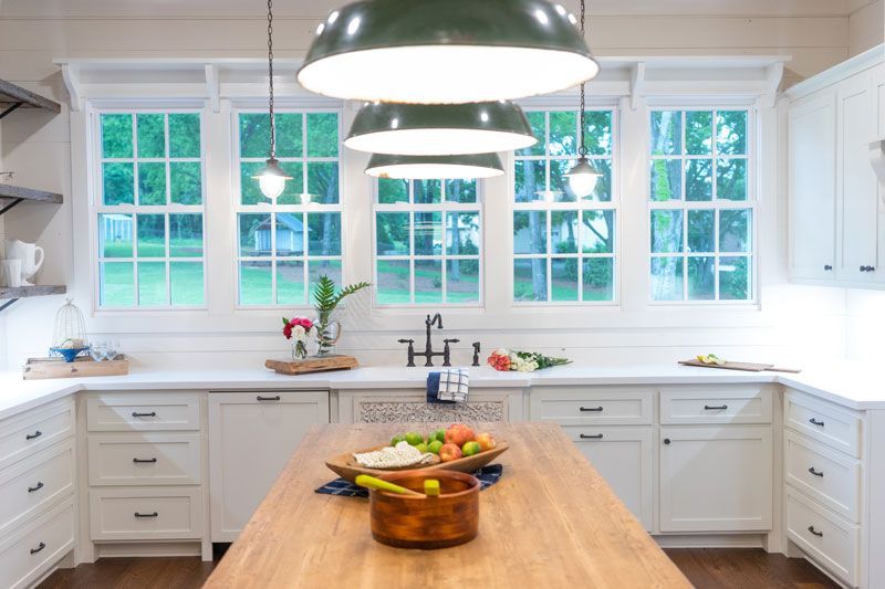 Bright white kitchen with large windows, farmhouse sink, and wooden island with fruit bowl and pendant lights