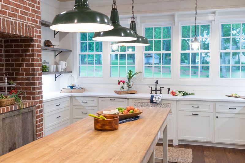 Bright kitchen with white cabinets, wood island, green pendant lights, and large windows