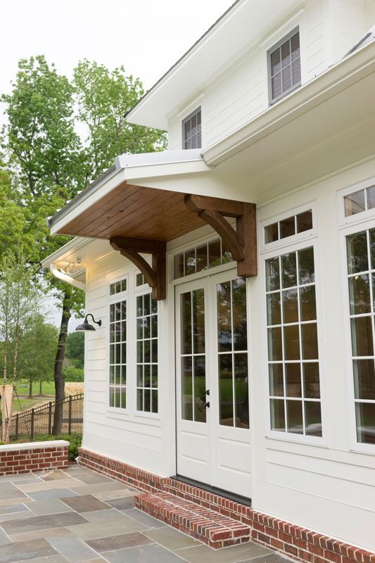 White house exterior with French doors, brick steps, and a wood awning over a stone patio.
