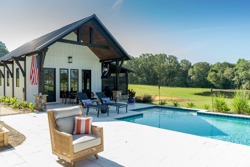 Modern house with a patio and lounge chairs beside a turquoise swimming pool and grassy backyard