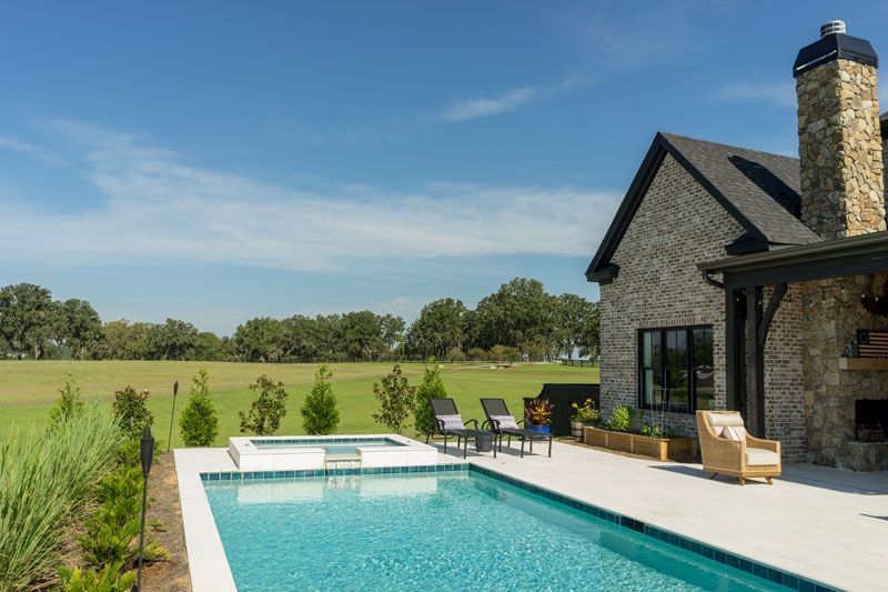 Modern stone house with patio and turquoise pool overlooking a green field under a clear blue sky