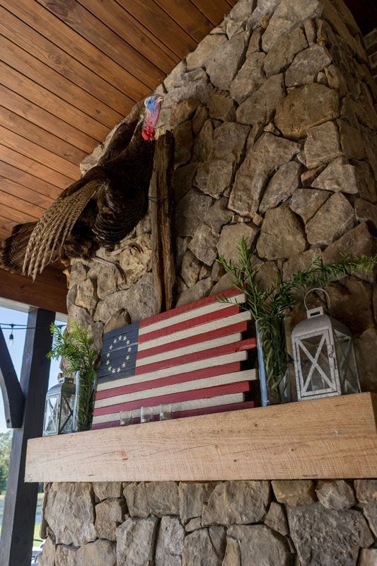 Wooden wall with stone chimney, American flag shelf, lantern, and a turkey perched near the ceiling.