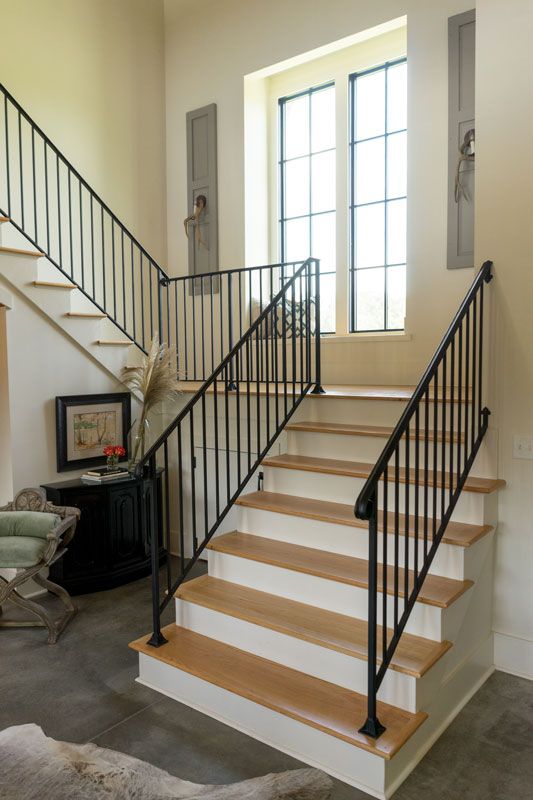 Interior staircase with black railings, light wood steps, and tall windows in a bright entryway