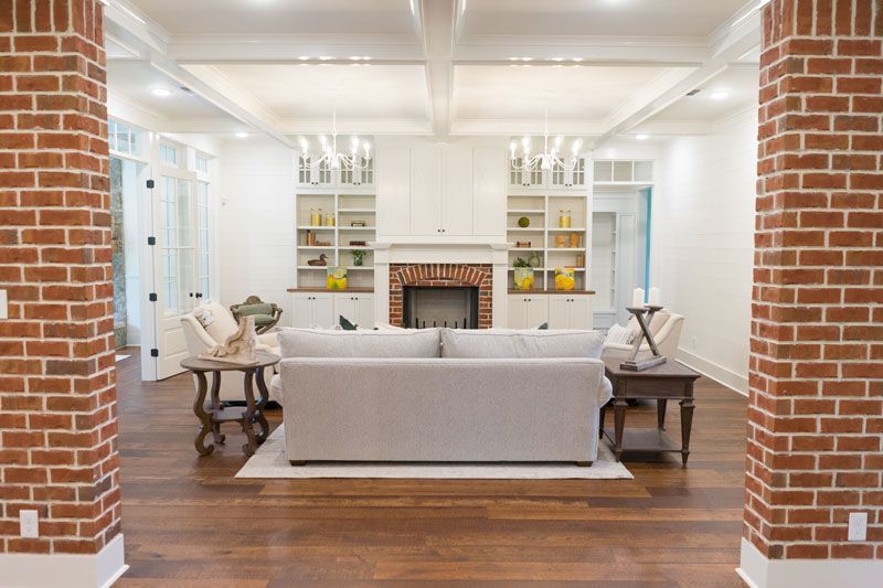 Bright living room with white sofas, brick pillars, hardwood floor, and a fireplace centerpiece